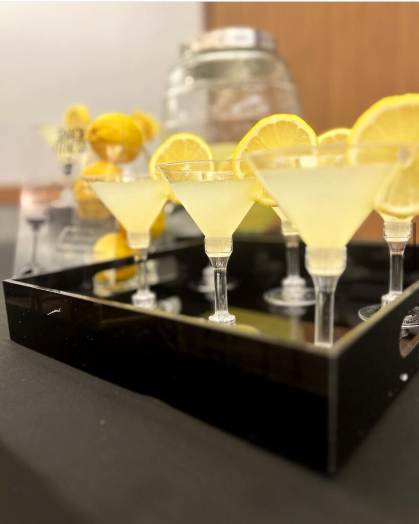 Beautiful bar setup for a Milwaukee event by On The Rocks Mobile Bartending of yellow lemon flavored martinis in clear glasses with a fresh orange slice garnish on the rim sitting in a black tray