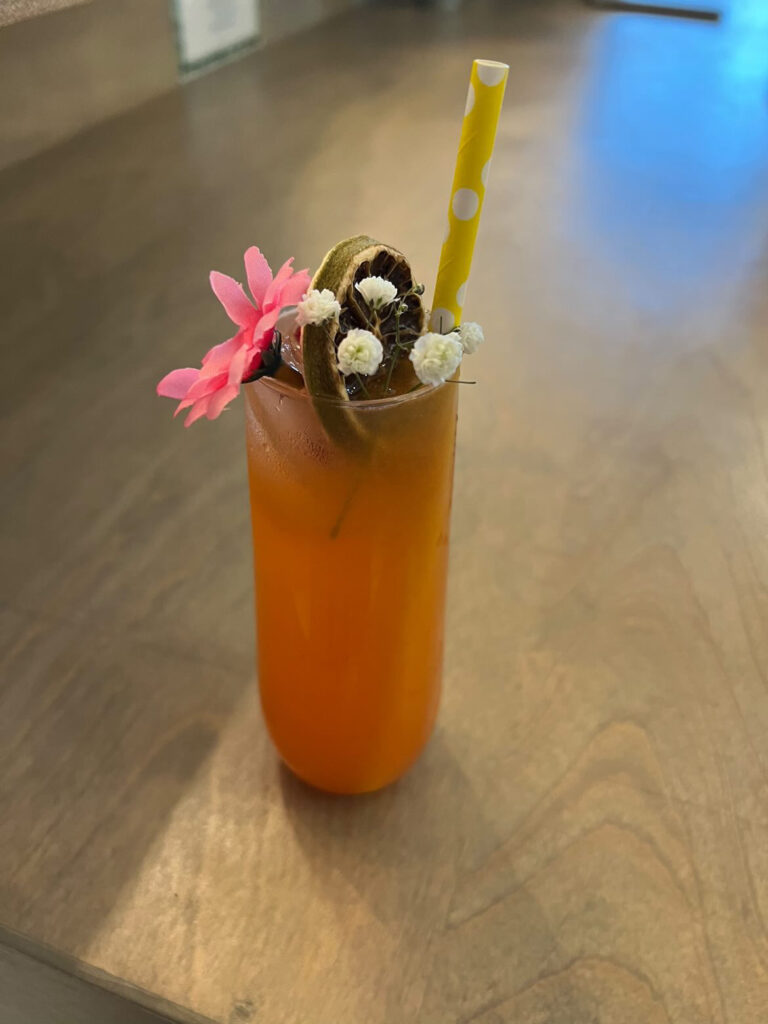 Close up view looking straight on of on an adorable cocktail created by On the Rocks Mobile Bartending Company in Milwaukee, WI for a networking event with a yellow paper straw with white polka dots, dried fruit garnish, pink flower and babies breath toppers in a clear glass