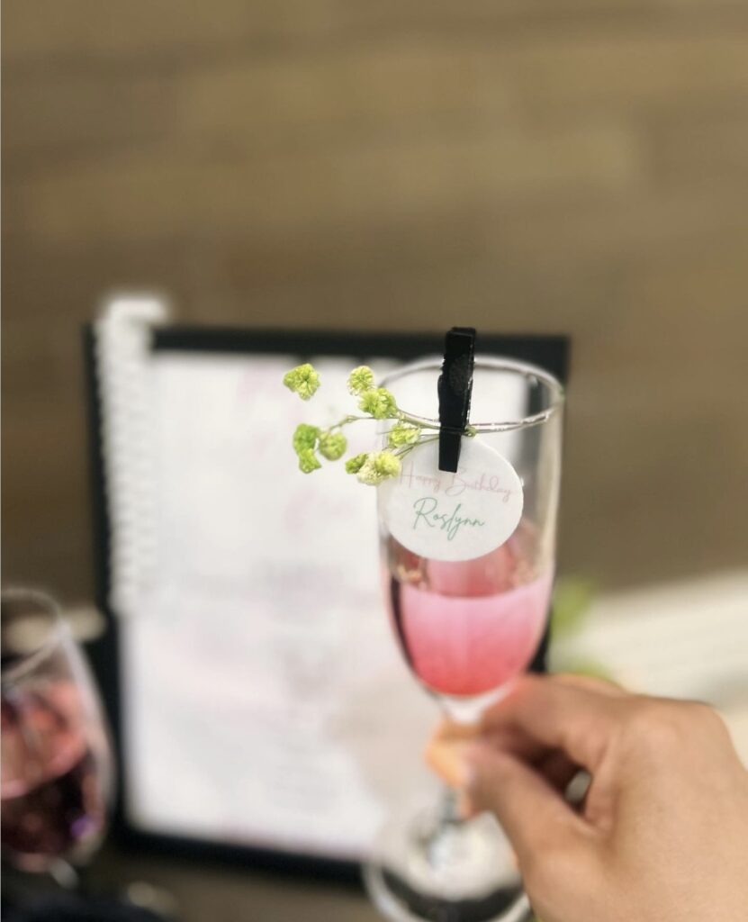 Rosé with small sprig of green baby's breath flowers and "Happy Birthday Roslynn" paper logo pinned to the rim, a gorgeous custom made look for a private event